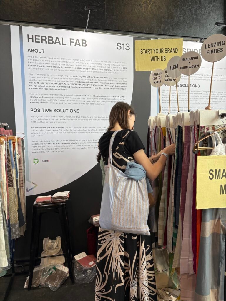 Woman browsing sustainable fabric swatches at the Herbal Fab booth during an international textile and fashion exhibition